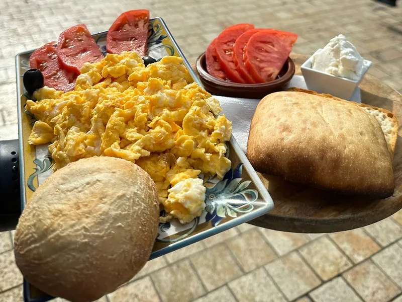 Scrambled eggs with sliced tomato, fresh cheese and two bread rolls, held over the paving of Plaza de la Merced