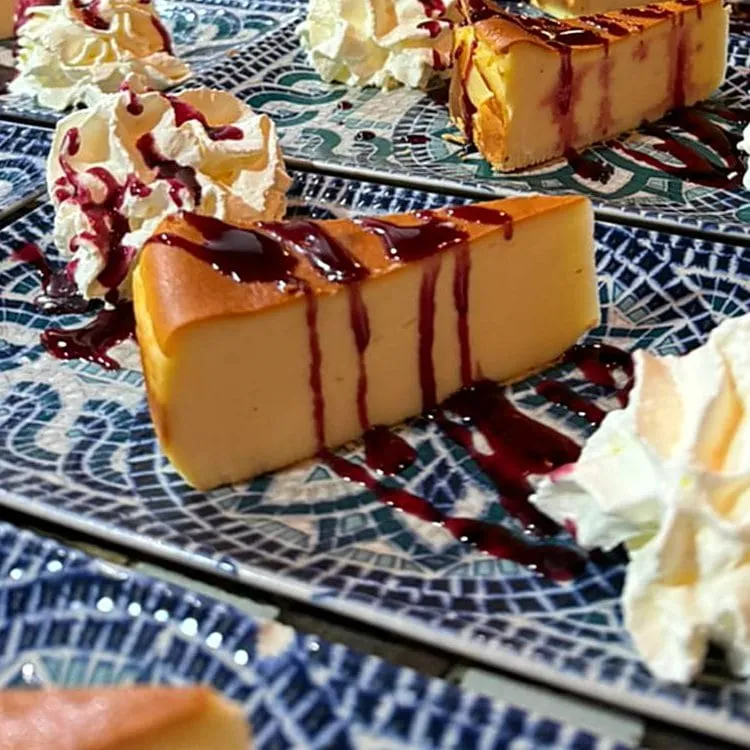 A slice of cheesecake with berry sauce and whipped cream on a blue-patterned plate