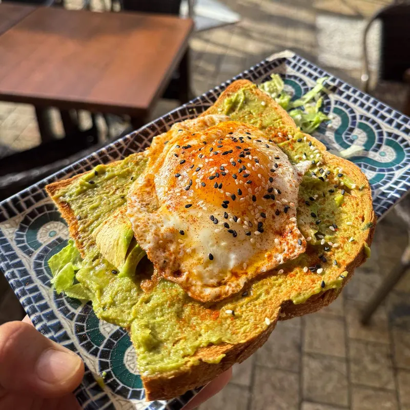 Avocado toast topped with a fried egg, paprika and sesame seeds on a mosaic plate